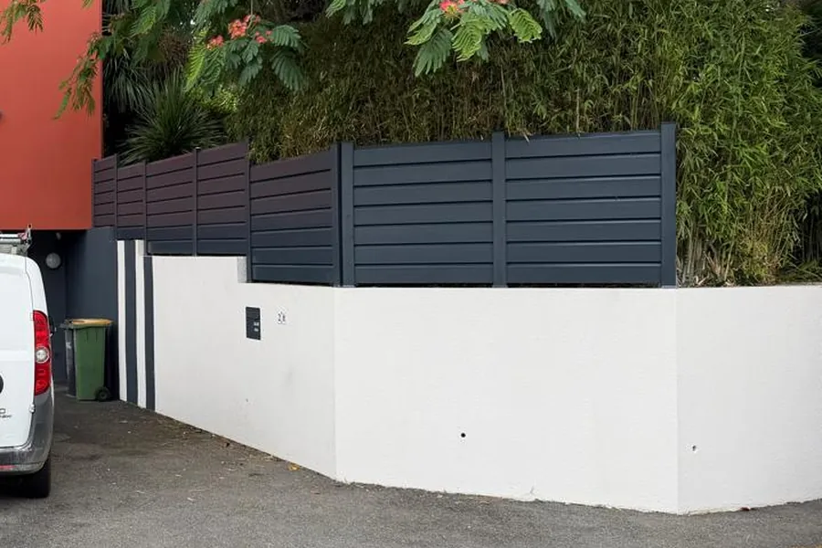 Mur de clôture repeint en blanc et façade d'immeuble rouge brique traitée par JMI Rénovation